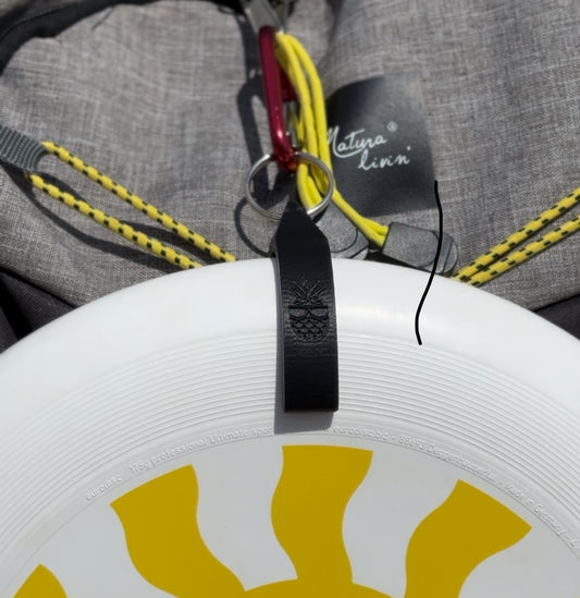Close-up of a white frisbee with yellow design, black strap, and gray bag in the background.